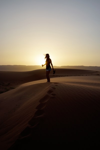 女人站在沙子在日落
